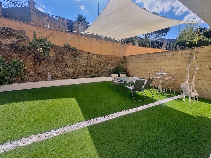 Jardín con césped, mesa exterior y vela de sombra para comer al aire libre.