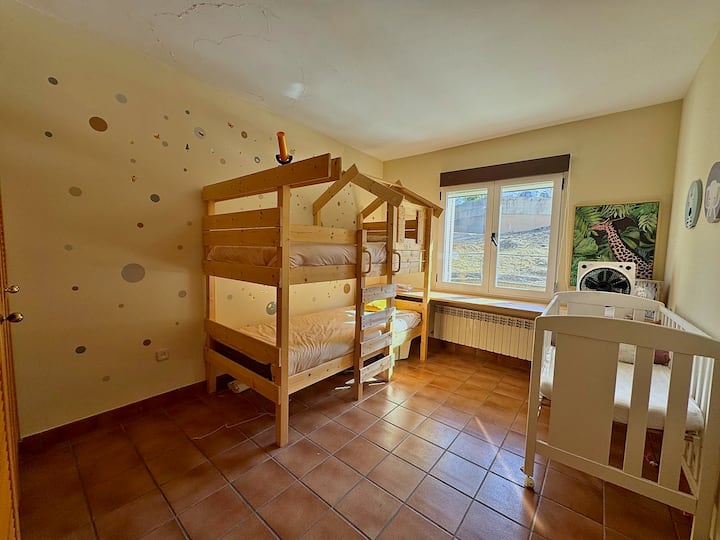 Dormitorio infantil con litera tipo casita y escritorio junto a la ventana.
