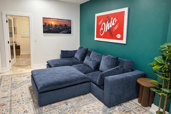 Sala acogedora con un sofá seccional cómodo, una pared decorativa llamativa y obras de arte locales