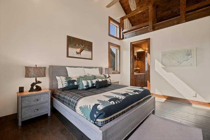 Vaulted ceilings and rustic lodge accents set the tone in this king bedroom, complete with an ensuite bath and an elk portrait overhead — a peaceful retreat filled with natural mountain light.