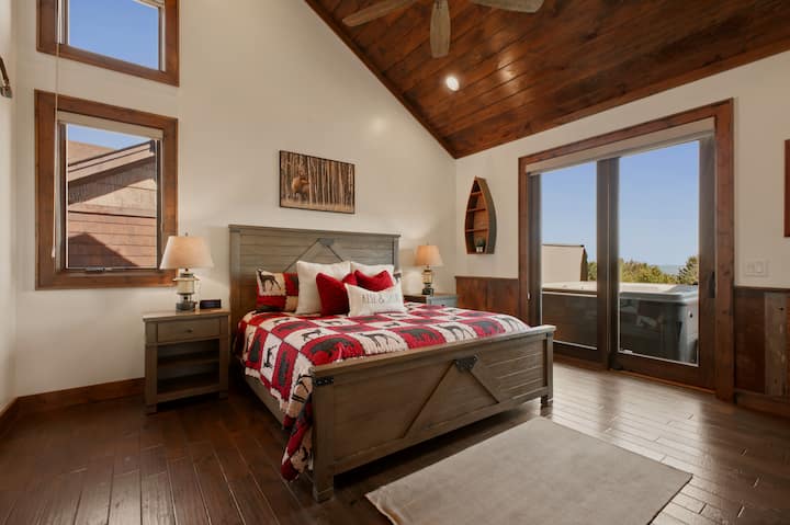 A soaring vaulted ceiling tops this king bedroom, where sliding glass doors open directly onto a private hot tub — bold plaid bedding and woodland art add rustic flair to this main-level retreat.
