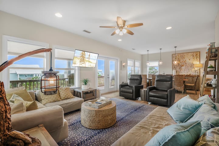 Spread out after a beach day: someone on the sectional, someone at the table, the deck doors open to the breeze. One big open room, so nobody misses the story.