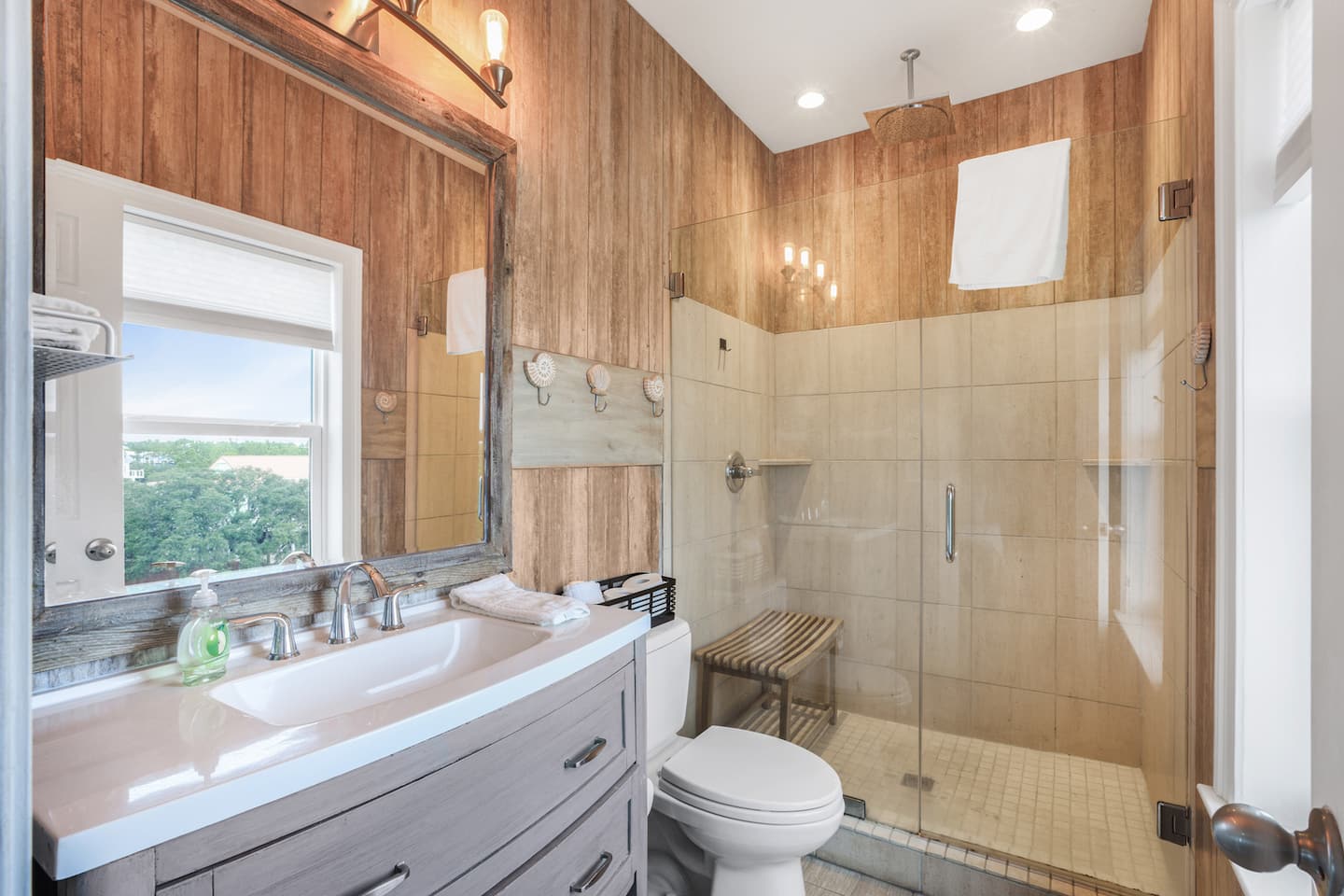 Step into the walk-in glass shower after a day in the sun: plank walls, a bench to sit on, and a window so you can still see the sky.