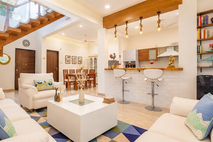 The living room offers cozy seating, a chic coffee table, and colorful accents that bring personality to the space. The adjoining dining area is perfect for shared meals, while the modern kitchen counter and bar stools create a relaxed spot.
