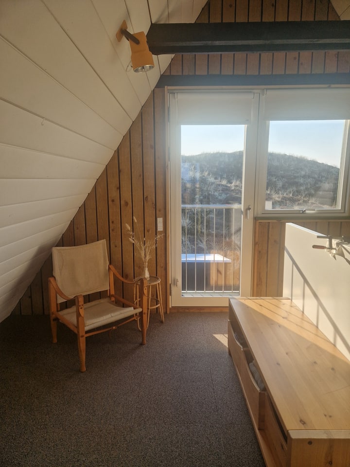 Основна спалня с легло 140×200 и изглед към дивата природа зад къщата и сутрешното слънце.