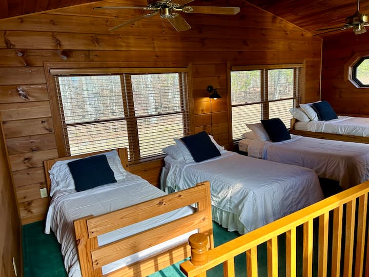 Four single beds are in the loft along with a bookshelf, a chair and a mirror.