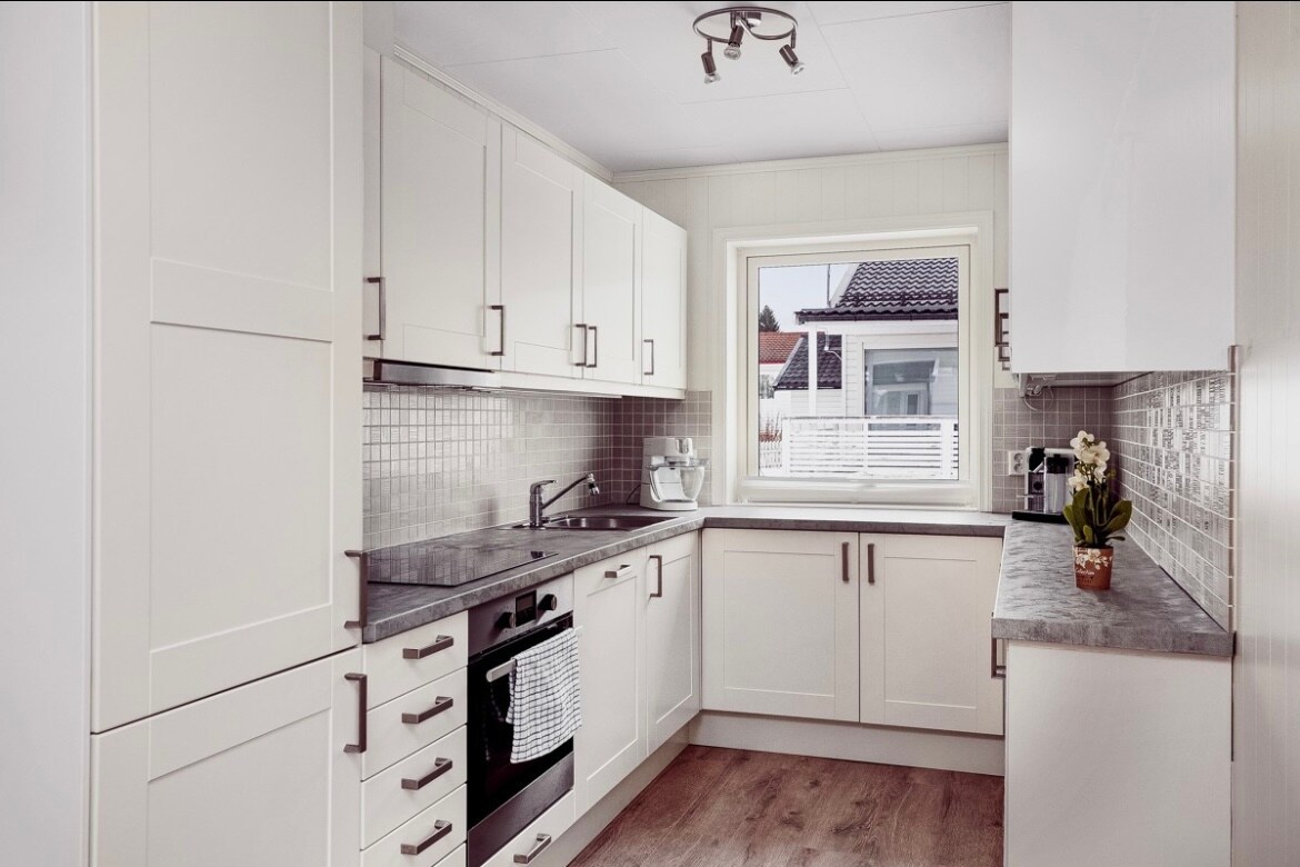 A modern kitchen is displayed, featuring light-colored cabinetry and sleek, gray countertops. Stainless steel appliances are positioned for convenience, while a window allows natural light to illuminate the space. A subtle tile backsplash complements the overall design, enhancing a clean and functional atmosphere.