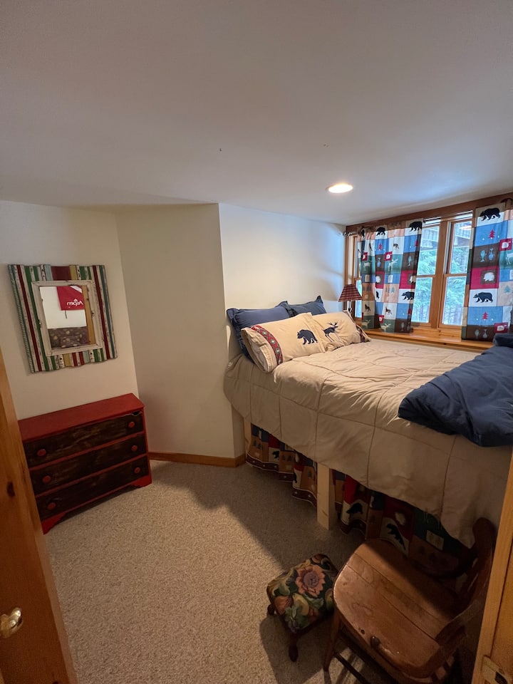 Тази уютна спалня разполага с двойно легло на таванско ниво до телевизора в сутерена. 