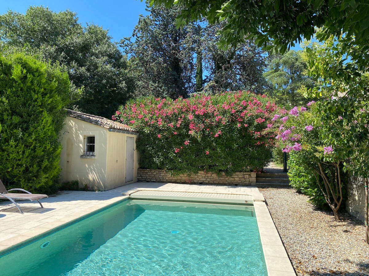 A private swimming pool is set within a spacious garden, surrounded by vibrant greenery and blooming flowers. A poolhouse sits nearby, while sun loungers are positioned on the poolside. The area is designed for relaxation and enjoyment in a tranquil outdoor setting.