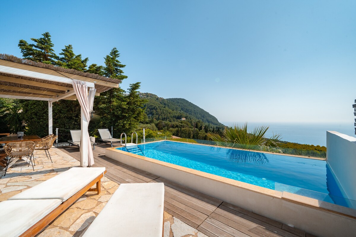 A serene outdoor space is depicted, featuring a pool with a gentle gradient that reflects the sky. Surrounding greenery adds to the tranquil atmosphere. Comfortable loungers are positioned beside the pool, while a pergola with draped fabric provides shaded seating for relaxation.