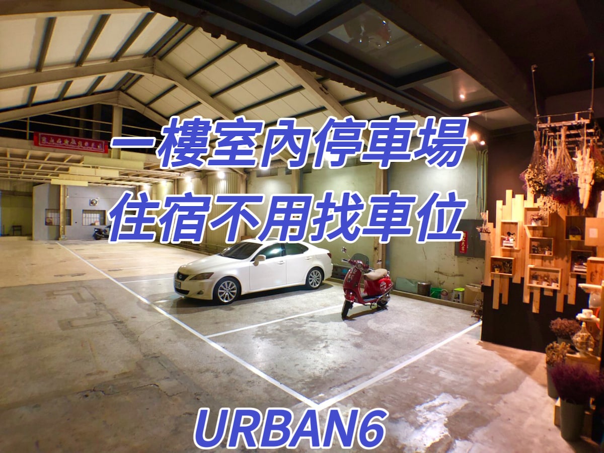 An indoor parking area is displayed, showing several designated parking spaces with clear floor markings. Natural lighting enters through windows, illuminating the spacious design. A car and a scooter are parked within the designated spots, highlighting the convenience of on-site parking for guests.