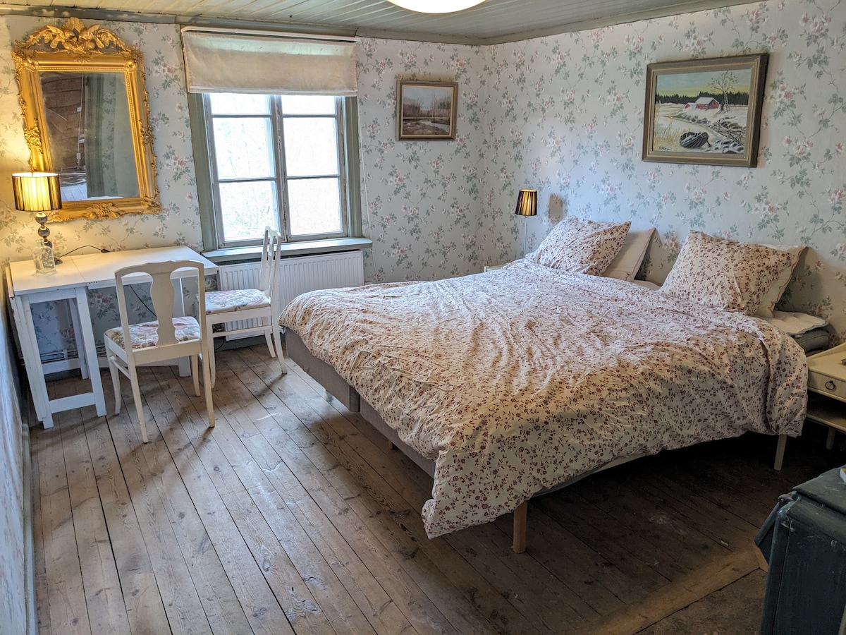 This cozy bedroom combines country charm with comfort.  Here you will find a spacious double bed, surrounded by floral wallpaper and beautiful antique details.  A perfect room for relaxation with natural light and harmonious atmosphere.