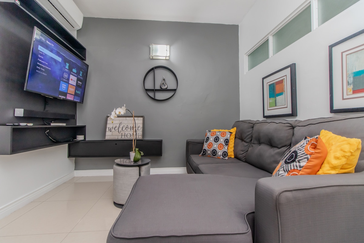 Opustite se u našem udobnom i suvremenom dnevnom boravku s otomanskim stolom/sjedalom, kaučem na razvlačenje (bračni krevet), 4K 4K Ultra HD Smart TV-om s kabelskom televizijom (Digicel), zvučnim barom