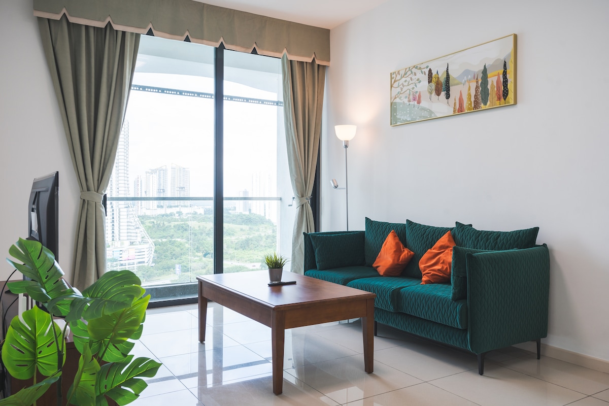 A living area is presented with a green couch adorned with orange cushions, complemented by a wooden coffee table. Floor-to-ceiling windows offer expansive views of the surrounding landscape. Light curtains frame the windows, and a floor lamp provides additional illumination.