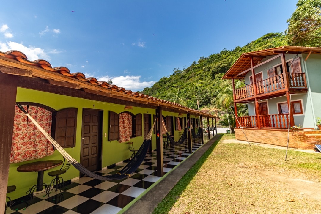 The exterior of the property features a charming layout with two buildings. One is a two-story structure with balconies, while the other displays a series of ground-floor suites. Hammocks are hung in front of the suites, and a grassy area complements the overall setting.
