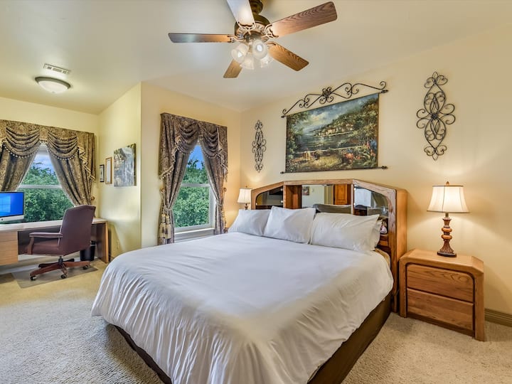 Upper floor king bedroom with desk, flat screen tv, balcony overlooking Lake Travis, power/usb connections on both sides of the bed, and ensuite bath (note that bedspread may be a different color)