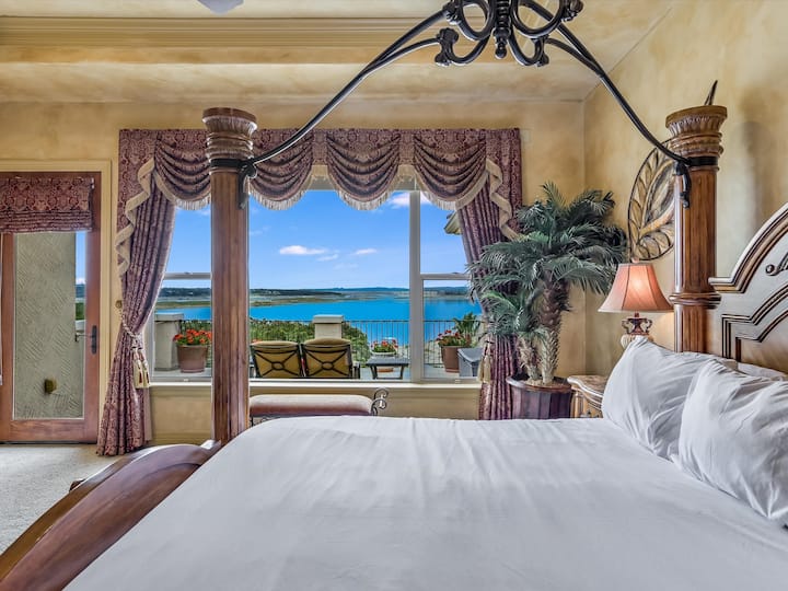 Upper floor primary bedroom with king bed, flat screen tv, large balcony, power/usb on both sides of the bed, ensuite primary bath, and amazing views of Lake Travis (note that bedspread may be a different color)