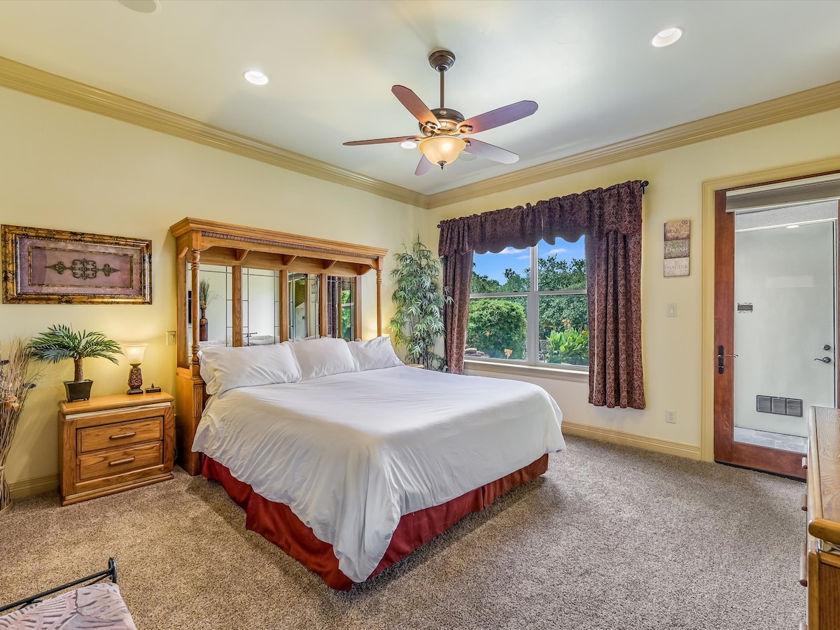 Chumba cha kulala cha Lakefront Suite (ngazi ya chini) chenye kitanda aina ya king, kabati kamili, runinga ya skrini bapa, soketi ya umeme/usb pande zote mbili za kitanda, mlango wa ufikiaji wa baraza, bafu la chumba, na mwonekano wa baraza la nyuma, beseni la maji moto na Ziwa Travis (kumbuka kwamba kitambaa cha kitanda kinaweza kuwa na rangi tofauti)