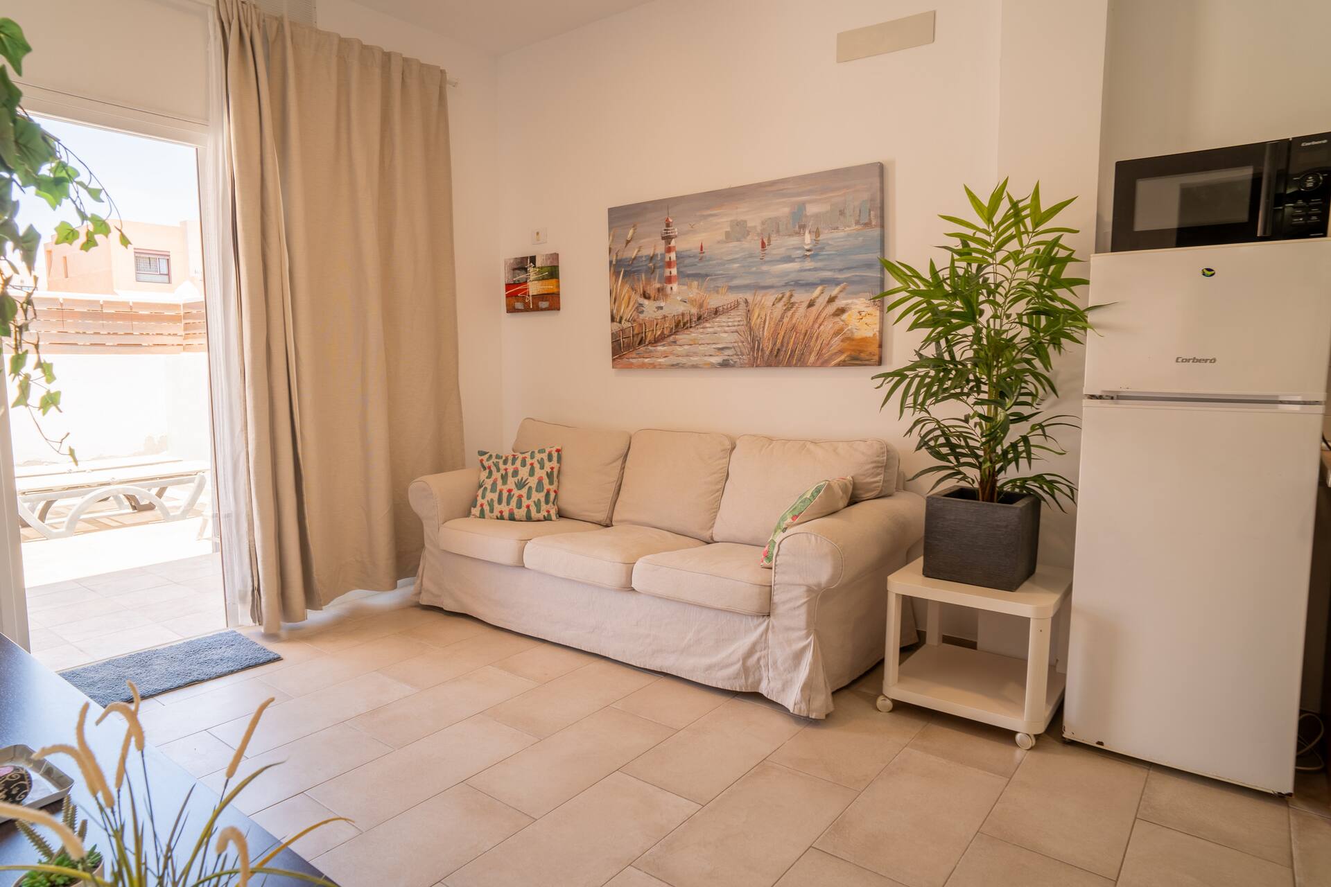 Salón luminoso con sofá amplio, cuadro marinero y nevera: acogedor y con aire canario.