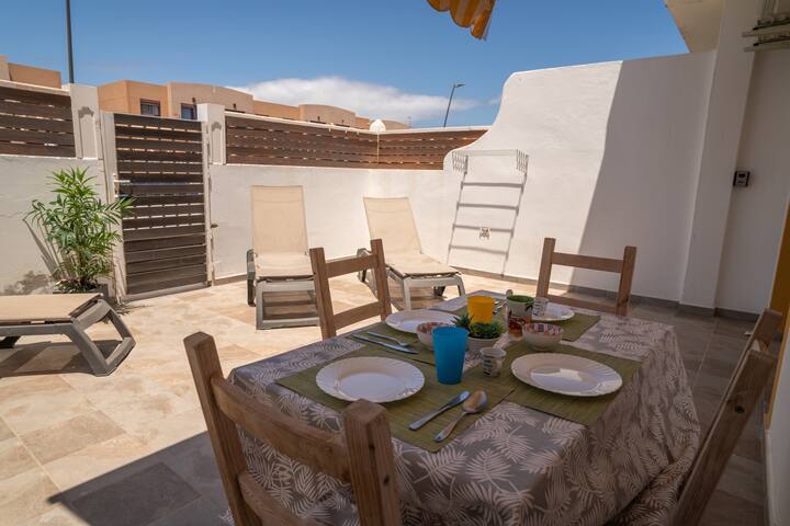 Comedor exterior en la terraza con mesa puesta: comidas al aire libre bajo el sol.
