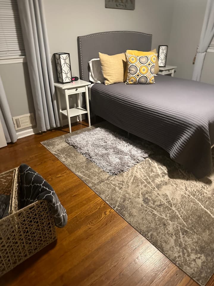 זה חדר השינה הראשי עם מיטת קווין סייז. כיסא אחד, מגירת צ'סטר צהובה וארון לאחסון בגדים.