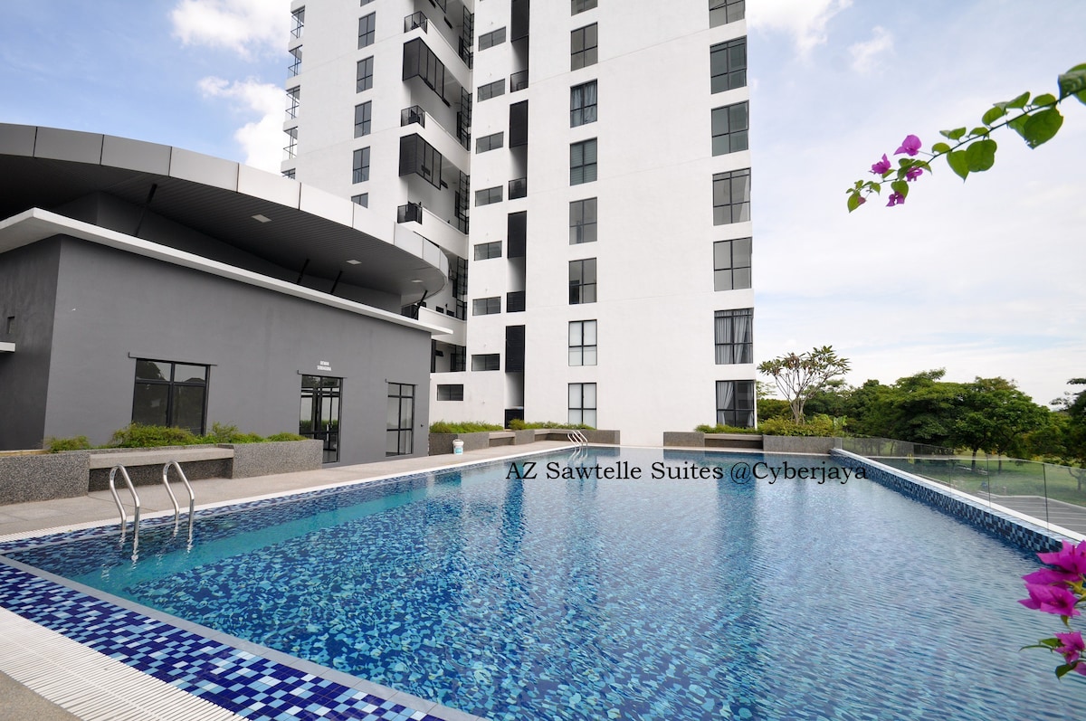 The swimming pool area features a clear blue surface with steps leading into the water. Surrounding greenery adds a natural touch, while the modern building stands adjacent, reflecting a contemporary architectural style. The pool is set within a tranquil environment.