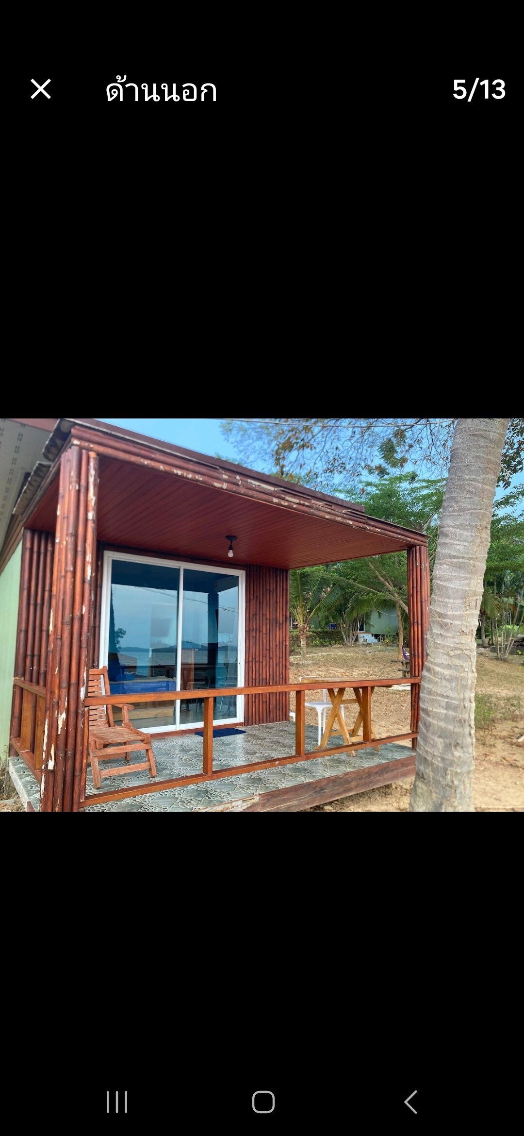 The exterior of a bungalow is showcased, featuring wooden paneling and a covered porch. A set of outdoor chairs and a small table are positioned on the porch, offering a cozy area to relax. Large glass doors provide views into the interior space.
