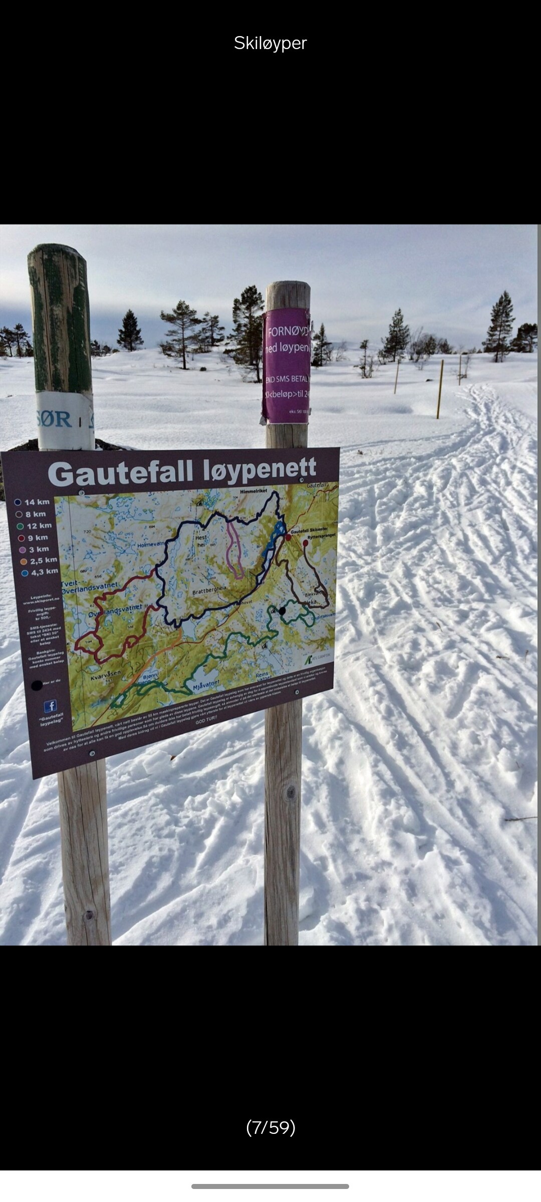 A trail map for Gautefall is displayed on a signpost, indicating various skiing routes. Snow-covered paths and trees are visible in the background, leading towards the horizon, offering a sense of the surrounding winter landscape.