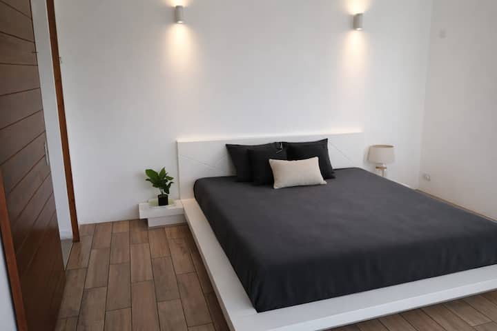 חדר שינה עם חלון מפרץ גדול המשקיף על המרפסת. נוף לגינה ולבריכה