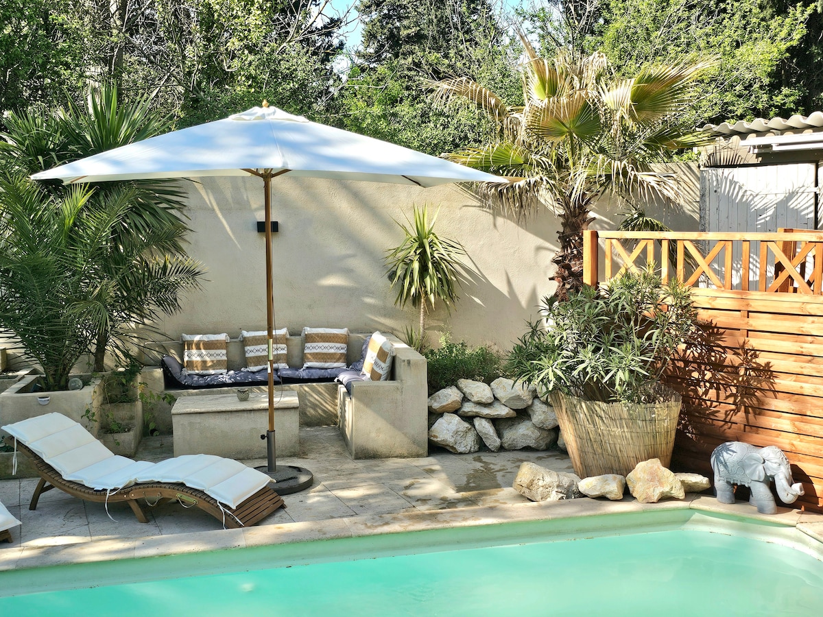 A private outdoor area is featured, showcasing a swimming pool surrounded by lush greenery and tropical plants. A shaded seating area with cushions is positioned beside the pool, and a sun lounger is placed nearby, creating a relaxing space for guests.