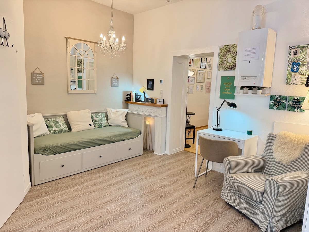 In einem Bereich der Wohnküche steht ein gemütlicher Lesesessel, ein Schreibtisch mit Schreibtischsessel, ein Deko Kamin und ein Tagesbett