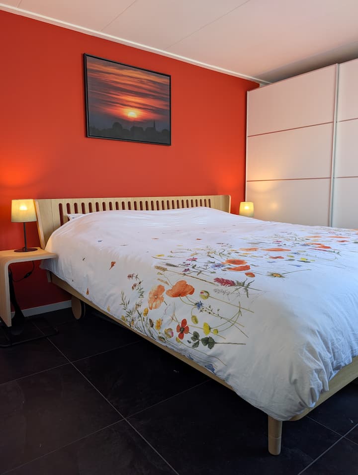 A finales de abril de 2026, habremos renovado la habitación por completo. Puertas de armario nuevas y una pared de color naranja/rojo cálido al atardecer, con vistas al pueblo de Langweer.