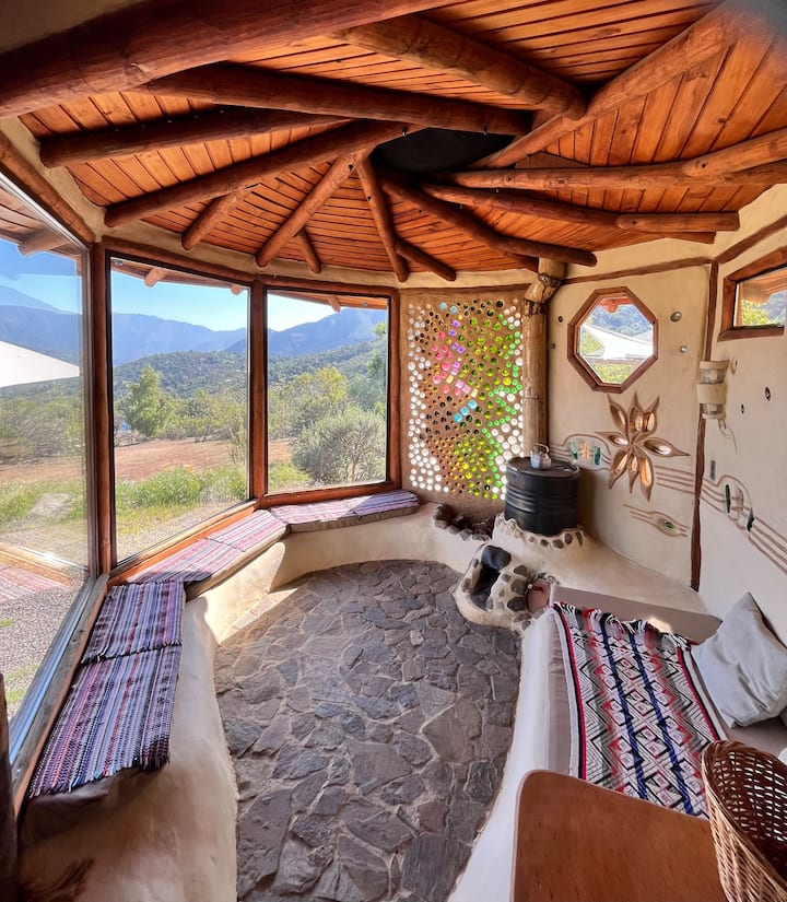 Living con bosca rocket muy calentita para el invierno. Con sofás que se calientan por la tubería de la bosca. Efecto de luz mágico con la pared hecha de 750 botellas recicladas. Vista panorámica sobre la Reserva de la Biosfera (montañas)