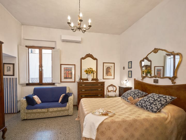 Charming vintage bedroom with a cozy double bed, classic wood furniture, bright natural light, and a comfortable sofa for relaxing.