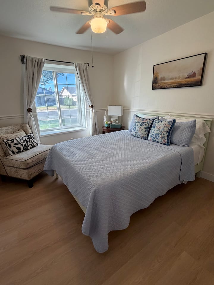 Bright and inviting, this queen bedroom features cozy bedding, natural light, and a comfortable reading chair—the perfect place to relax and recharge.