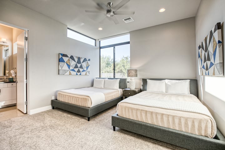 Elegante dormitorio en suite con dos camas tamaño queen, obras de arte modernas, iluminación suave y tonos neutros acogedores.