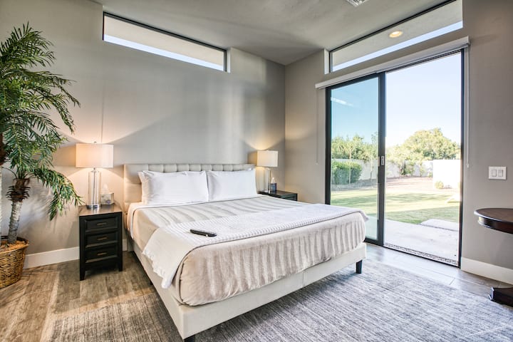 Serena casa de huéspedes con dormitorio tamaño king con puertas de vidrio del piso al techo que se abren a un jardín privado. La luz natural, los muebles modernos y las ventanas de travesaño crean un refugio lujoso.