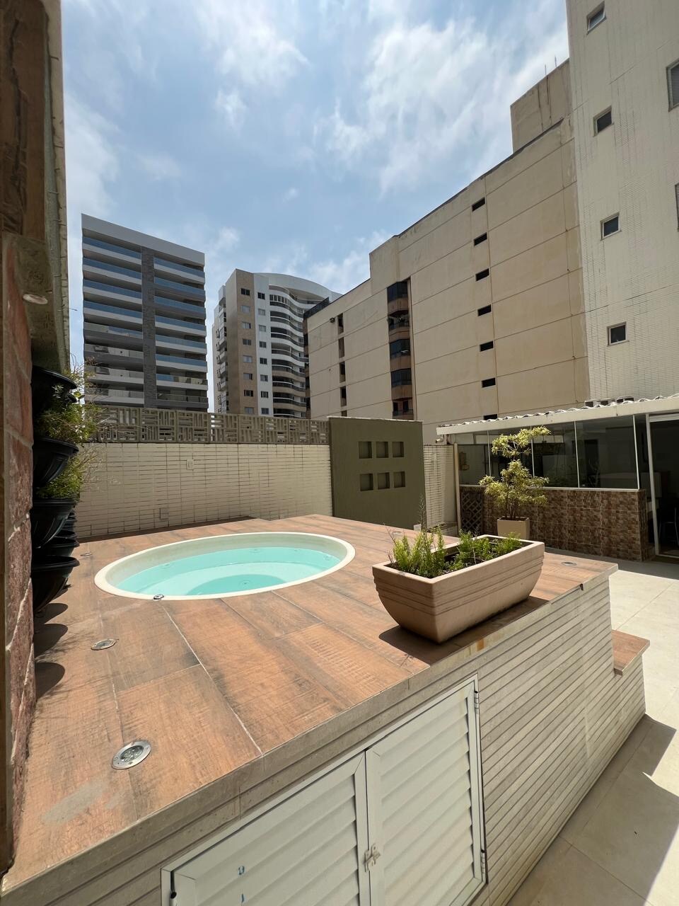 A private outdoor area is highlighted by a circular, heated jacuzzi, surrounded by wooden decking. Potted plants provide a touch of greenery, and the surrounding buildings create a contemporary urban backdrop. The space is designed for relaxation and enjoyment.