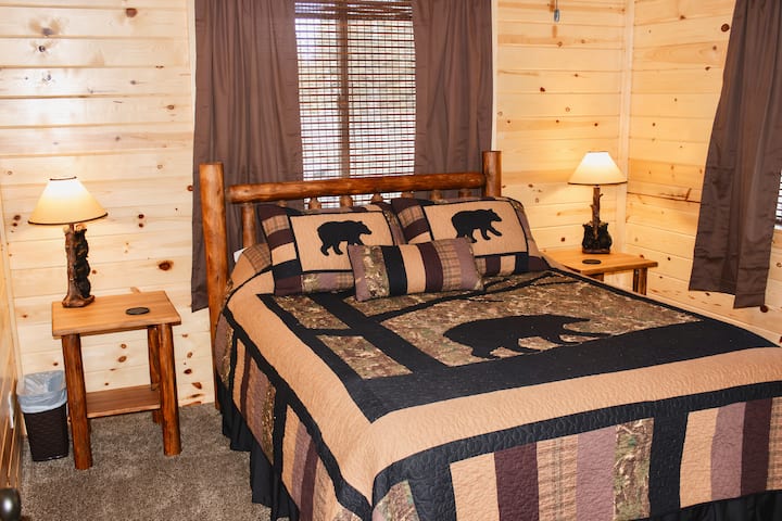 Cozy downstairs master bedroom featuring a queen log bed, warm wood interiors, and rustic bear-themed bedding for a comfortable retreat.