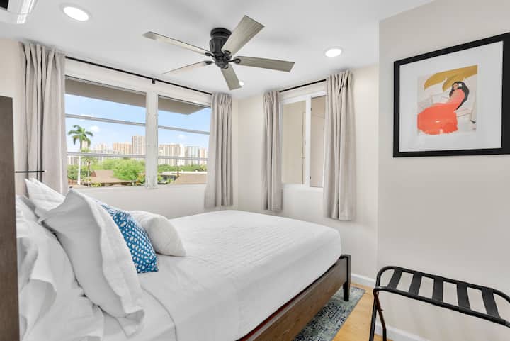 SECOND BEDROOM: Bright and inviting, this cozy bedroom features a queen bed sleeping up to two guests, multiple windows with blackout curtains for restful sleep, a ceiling fan, luggage rack and a discreet wall-mounted hanging hook for clothes.