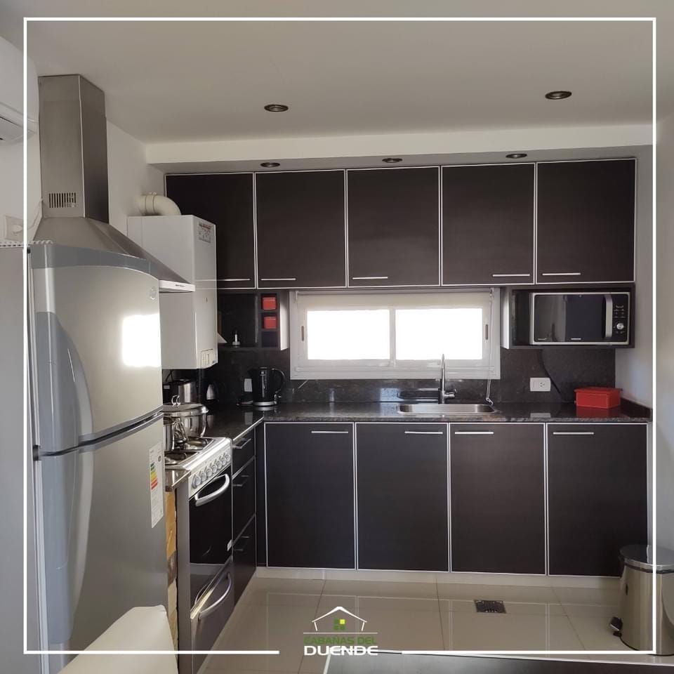 A modern kitchen is equipped with sleek dark cabinetry, stainless steel appliances, and a black countertop. Natural light enters through a window above the sink, enhancing the functional layout that includes an oven, stove, microwave, and ample storage space.