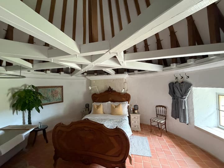 A first-floor beamed bedroom with a ten-metre turreted ceiling features an antique bed and a freestanding roll-top bath with Lefroy Brooks shower. The WC is tucked one level below, off the sitting room.