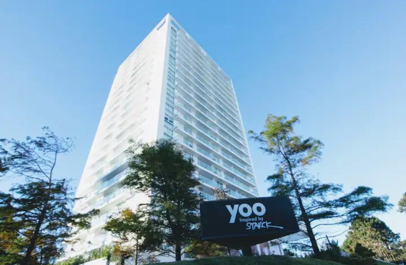 A modern high-rise building showcases a sleek design with multiple floors and large windows. Green trees flank the structure, emphasizing the natural surroundings. The prominent signage at the base identifies the property as Yoo, inspired by Space.