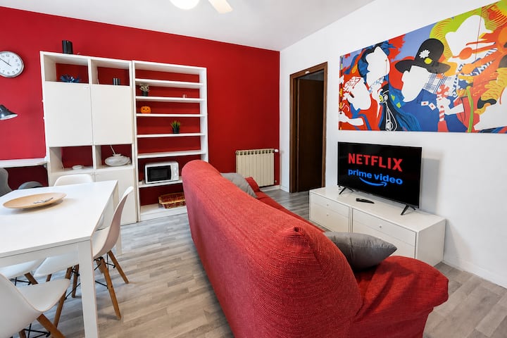 Un accogliente soggiorno con un divano rosso, scaffali bianchi e una TV 4K su una parete rosso acceso.