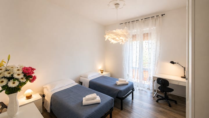Soveværelse med to enkeltsenge, en kommode og en garderobe med udsigt over en anden altan, der vender mod øst. Dette værelse har også en arbejdsplads med et bord, en stol og en lampe til at arbejde ved.