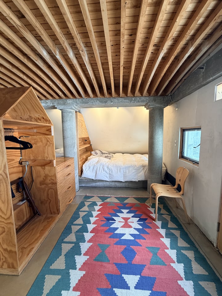 Dormitorio del tercer piso, tiene un cama tamaño queen que está cerca del suelo, en un espacio acogedor.