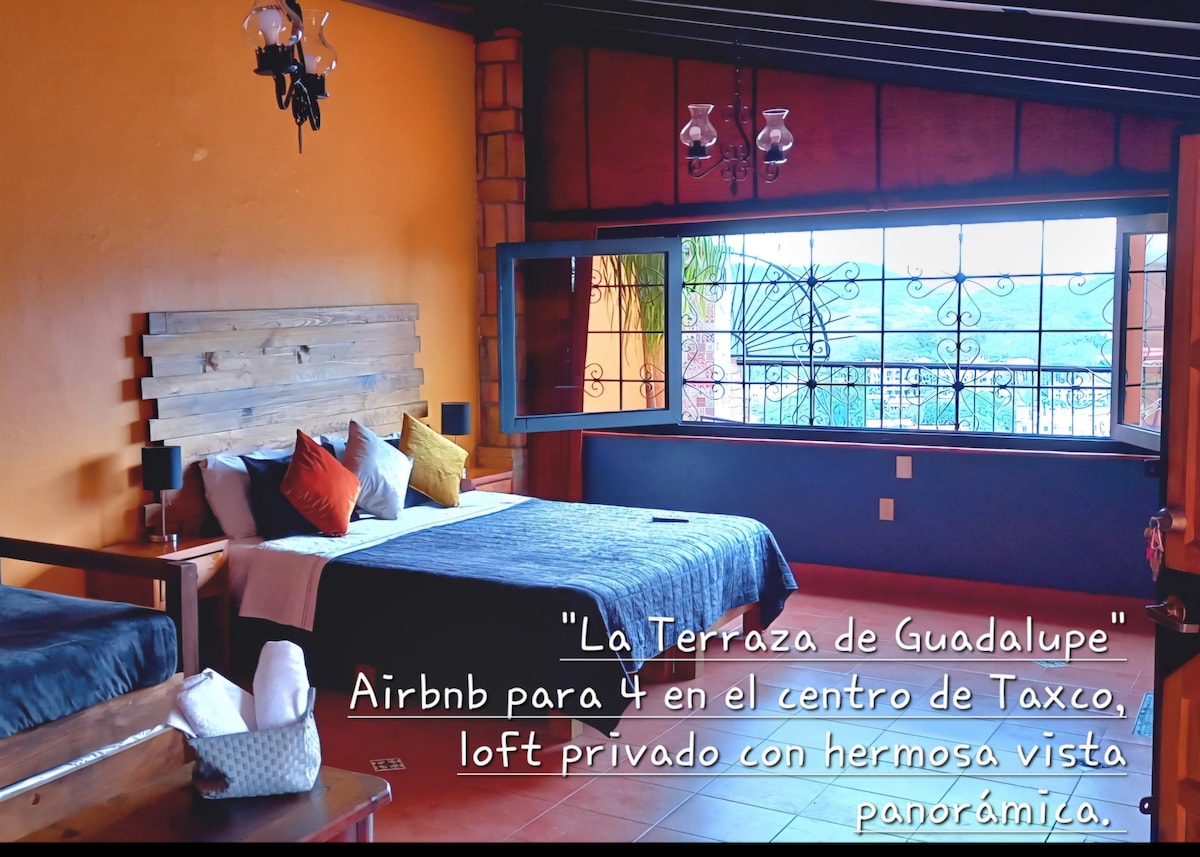 A spacious loft features a large king-size bed adorned with decorative pillows. A separate area contains two individual beds. Large windows provide panoramic mountain views, complemented by wooden accents and warm tones throughout the room. A cozy atmosphere is created by natural light pouring in.