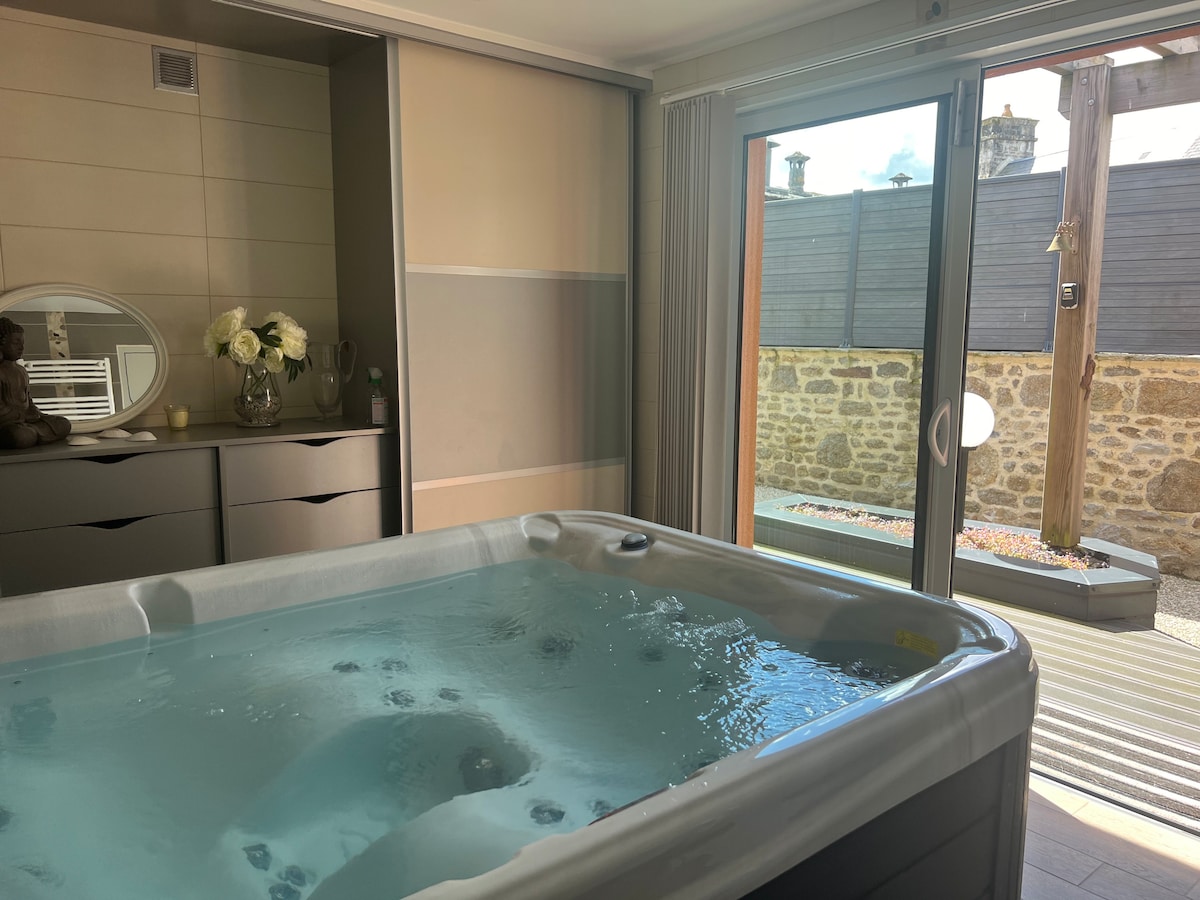 A spa area features a hot tub filled with clear water, positioned next to a sliding glass door that opens to a private outdoor space. Natural light floods the room, highlighting a neutral color palette and a decorative mirror on a nearby cabinet.