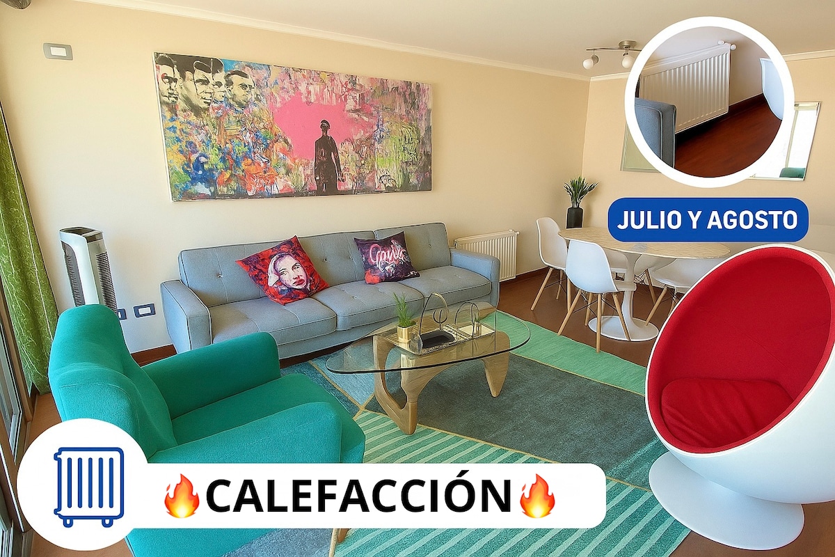 A modern living area features a gray sofa with colorful cushions and a glass coffee table. A vibrant piece of wall art is displayed above, while a striking Ball Chair adds a unique design element. A rug enhances the comfort of the space.