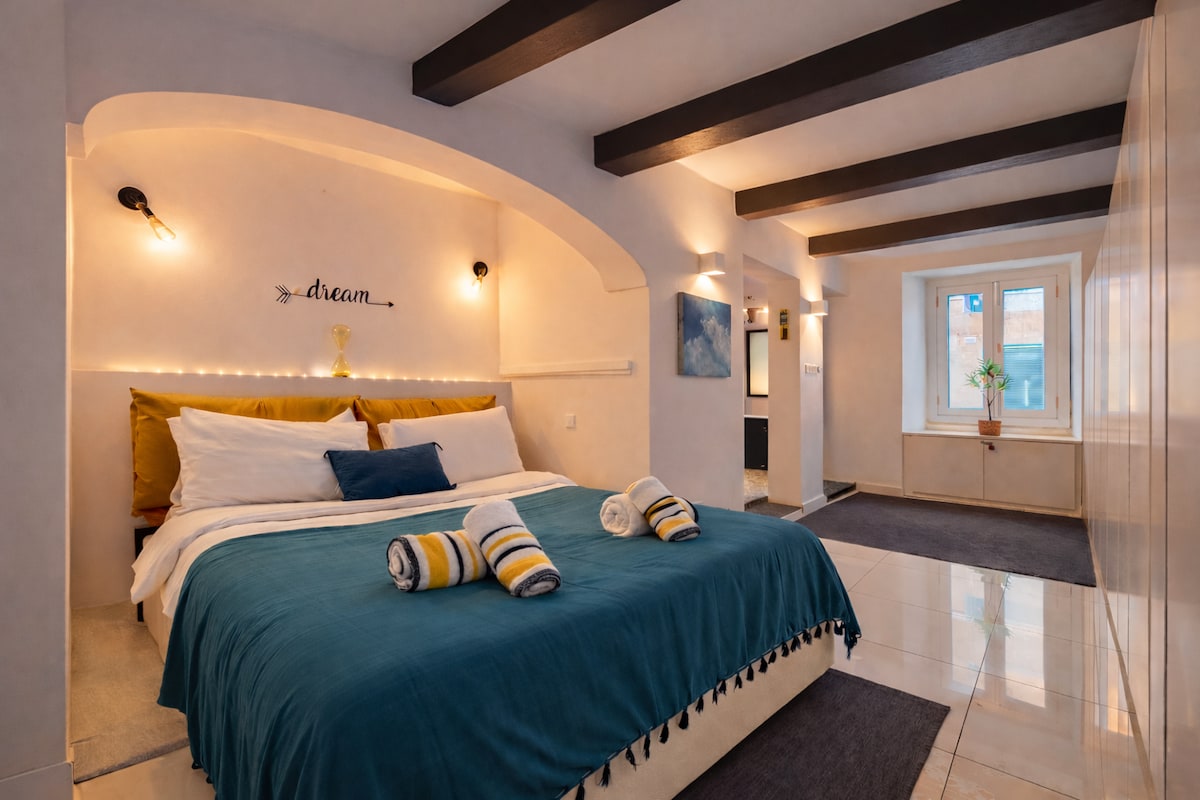 Спалната соба ве пречекува со меки сводови и видливи греди, како одраз на безвременскиот карактер на традиционалниот малтешки дом.